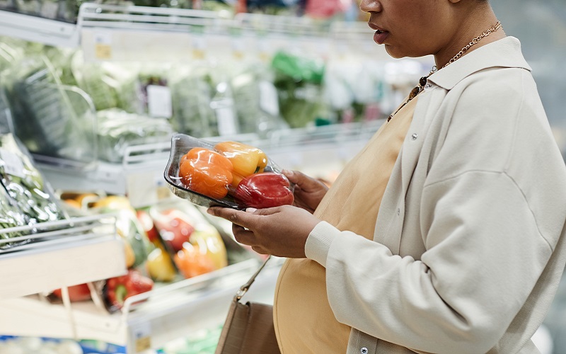 Cropped side view portrait of pregnant African-American woman buying groceries while shopping in supermarket